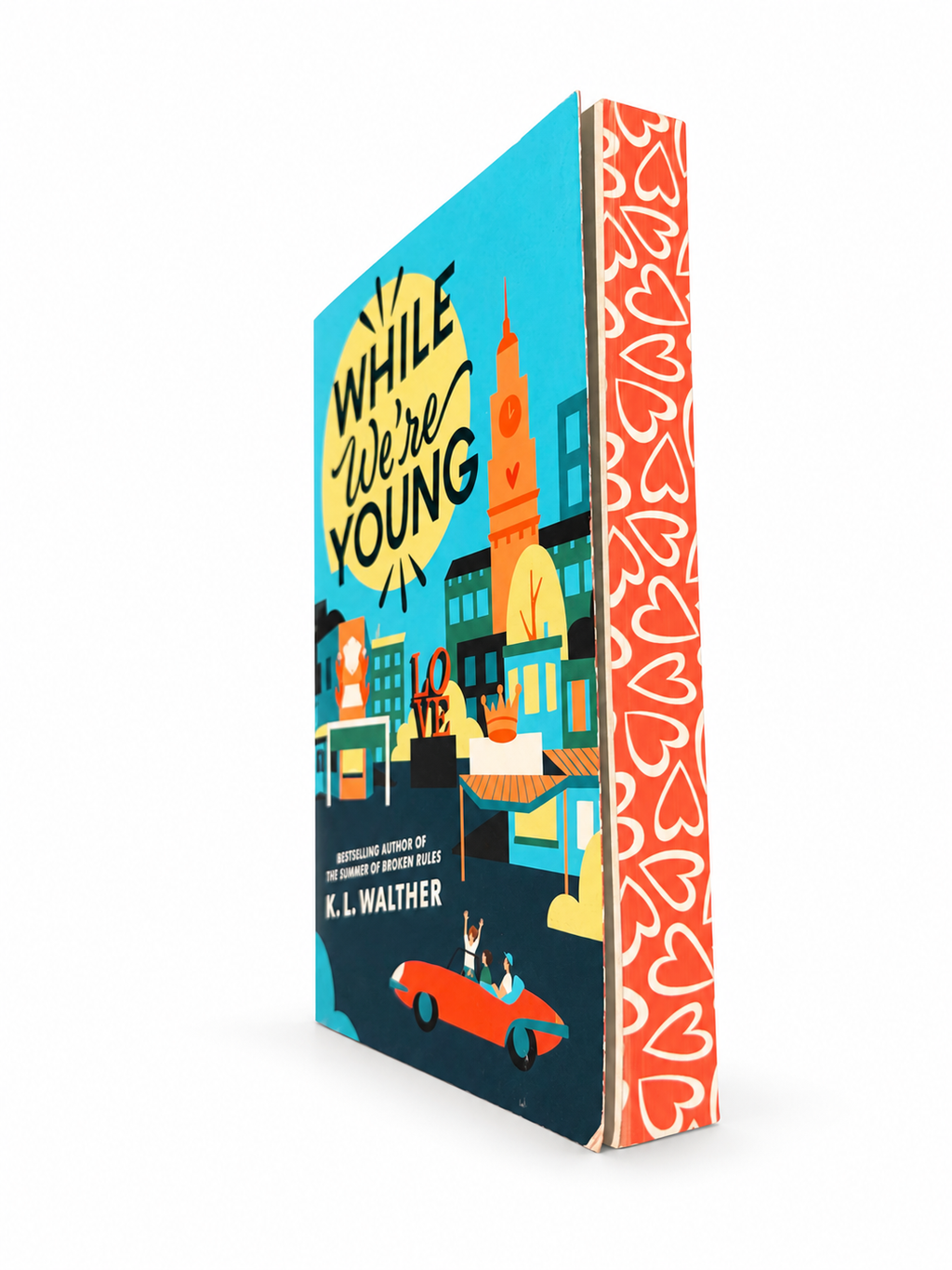 While We’re Young by K. L. Walther, shown at an angle with its heart-patterned spine against a clean white background.